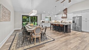 A modern kitchen with white cabinets, a stainless steel refrigerator, and a dining area with a wooden table and chairs. - Stunning Home, conveniently located in Raleigh (Raleigh)