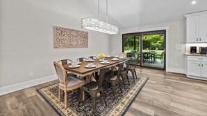 A dining area with a wooden table and chairs, a hanging light fixture, and a view of a garden through glass doors. - Stunning Home, conveniently located in Raleigh (Raleigh)
