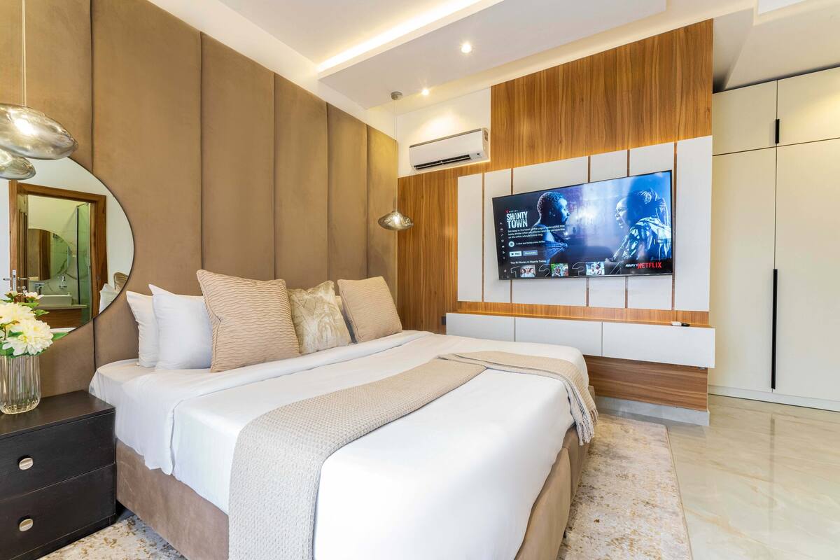 A modern bedroom with a large bed, a TV mounted on the wall, and a wooden panel design.