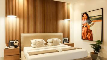 A modern bedroom with a wooden panel wall, a large bed with white bedding, two bedside lamps, a nightstand with a phone, a framed picture, and a potted plant.