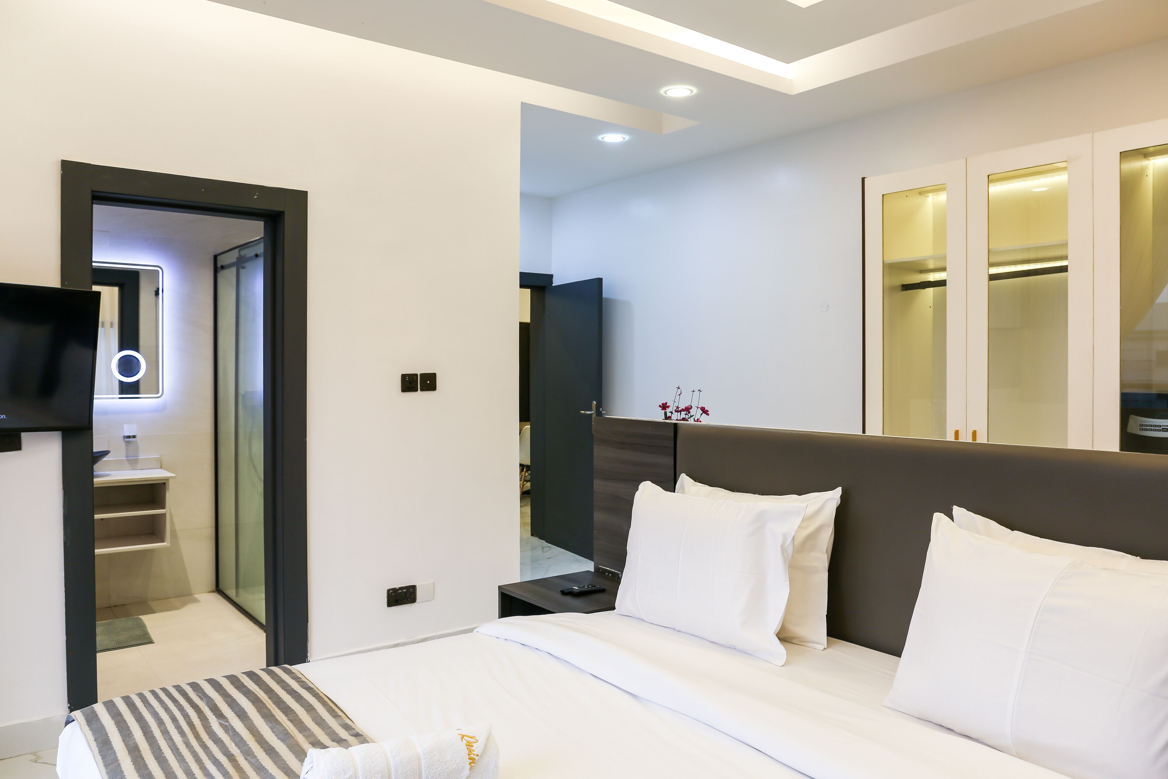 Ein modernes Hotelzimmer mit einem großen Bett, einem Nachttisch, einem Flachbildfernseher und einem begehbaren Kleiderschrank.