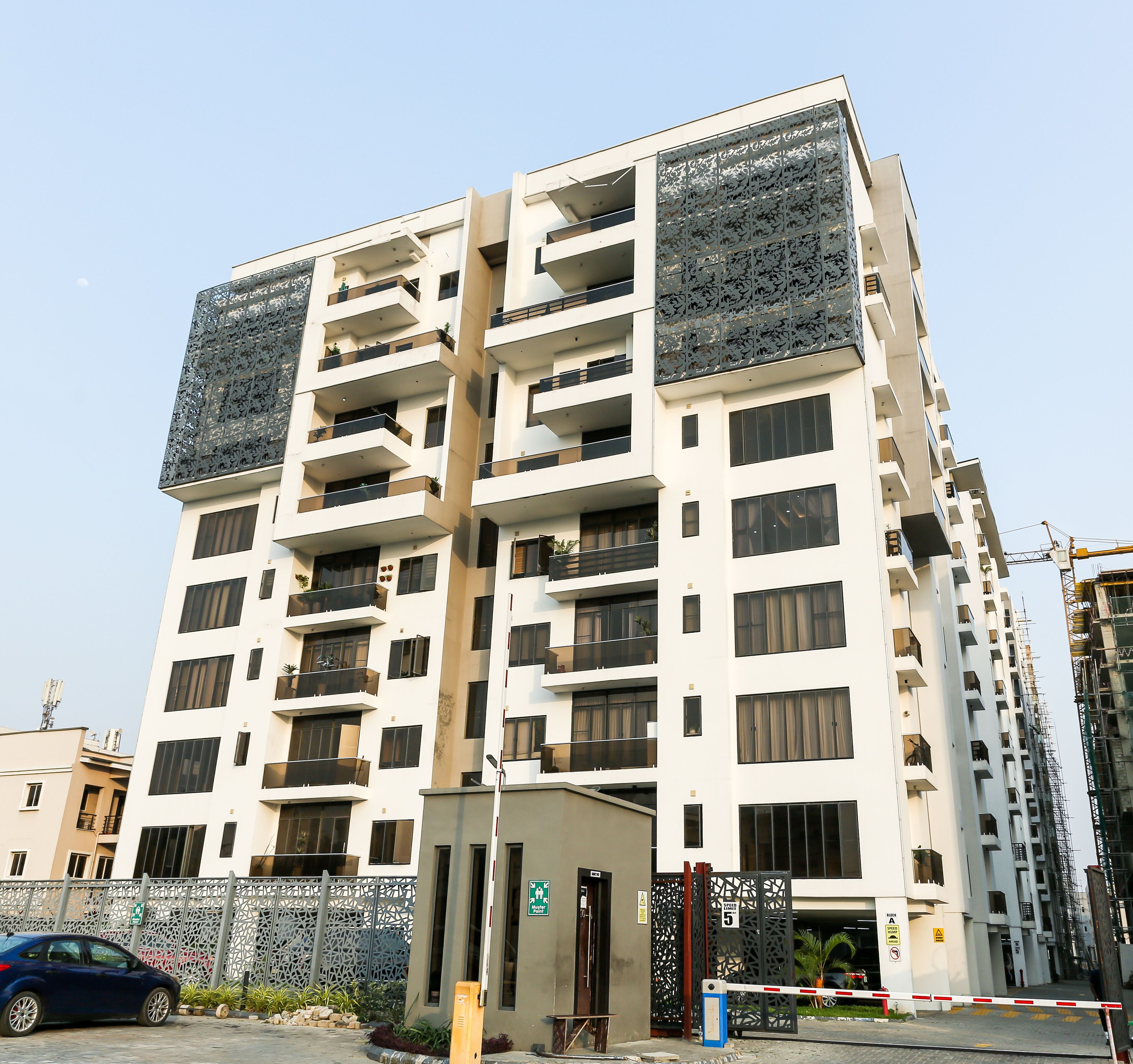 A multi-story residential building with balconies, a gated entrance, and a parking area.