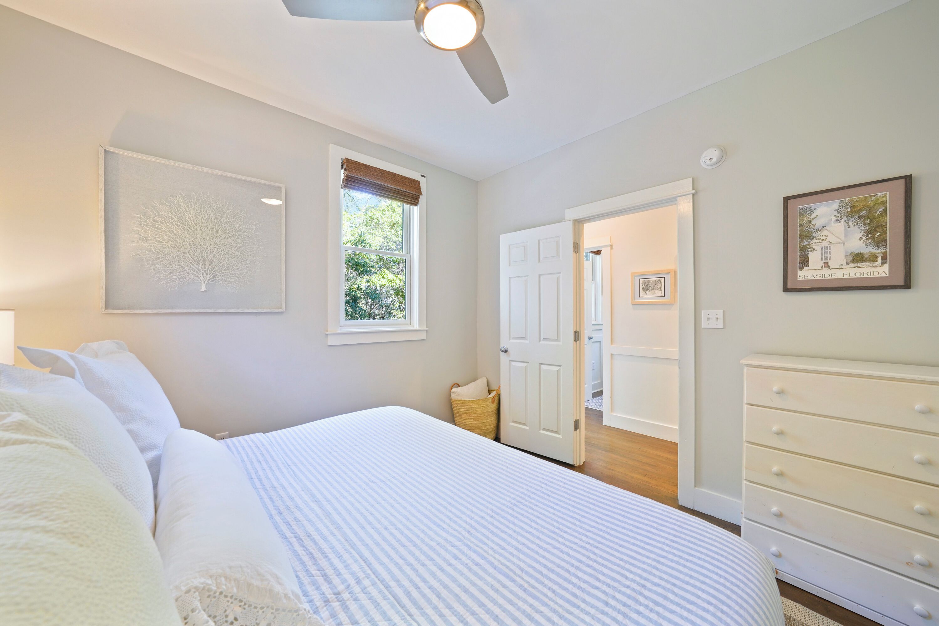 A bedroom with a bed, a dresser, a window with a view, and a door leading to another room.