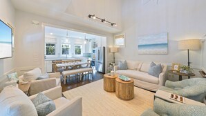 A spacious living room with a large sofa, a coffee table, and a dining area with a table and chairs. - Renovated in Seaside, Expansive Porches, 2 Kings, walk to Beach + 2 Bikes! (Santa Rosa Beach)
