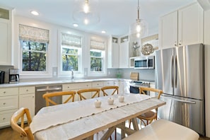 A modern kitchen with white cabinets, stainless steel appliances, and a wooden dining table.