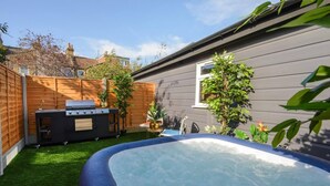 Un patio trasero con jacuzzi, una parrilla y una pequeña zona de estar.