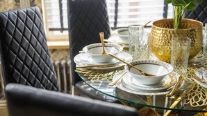 Una mesa de comedor dispuesta con platos blancos, cubiertos dorados y copas de cristal.