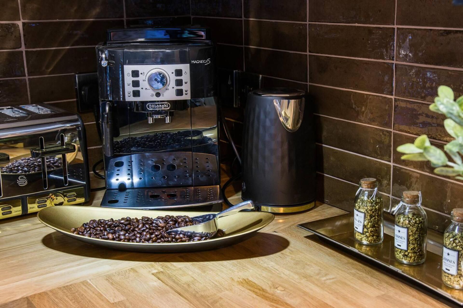 A coffee machine, a coffee pot, and a tray with coffee beans on a kitchen counter.