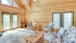 Interior de una cabaña de madera con sofá, dos sillones, una mesa y un pequeño banco de madera.
