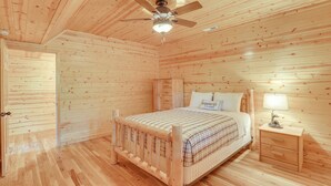 Un dormitorio con paneles de madera, una cama, una mesita de noche y un ventilador de techo.