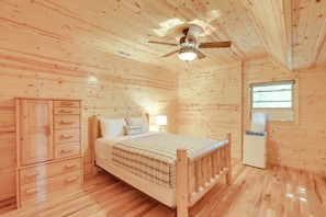 Ein Schlafzimmer mit Holzwänden, einem Bett, einem Kleiderschrank, einem Deckenventilator und einem Fenster.