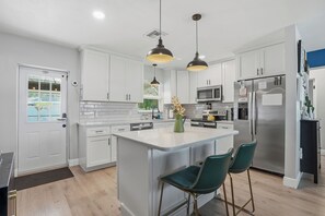 A modern kitchen with white cabinets, stainless steel appliances, and a central island with bar stools. - Private Heated Salt Water Pool Oasis • 10 Mins to Clearwater Beach (Clearwater)