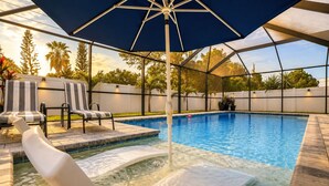 Un área de piscina con sillones de descanso, una bañera de hidromasaje y una sombrilla.