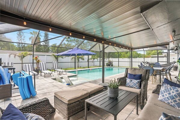 A covered outdoor area with a pool, lounge chairs, and a table. - Private Heated Salt Water Pool Oasis • 10 Mins to Clearwater Beach (Clearwater)