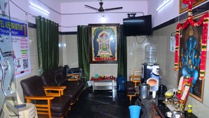 A room with a sofa, chairs, a television, a water dispenser, and a shrine. - Hotel Aishwariyam Thirukadaiyur (Tarangambadi)