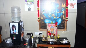 A reception area with a water dispenser, a framed deity image, and a check-in/check-out sign. - Hotel Aishwariyam Thirukadaiyur (Tarangambadi)