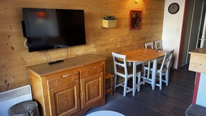 A cozy room with a wooden wall, a flat-screen TV, a wooden dining table with chairs, a small round table, and a cabinet. - T2-6pers-34m2-quartier Bergers-pied des Pistes (Huez)