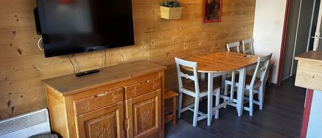 Une pièce chaleureuse avec un mur en bois, un téléviseur à écran plat, une table à manger en bois avec des chaises, une petite table ronde et un buffet.