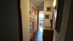 A narrow hallway with wooden flooring, a bench, and a small wooden table with a mirror and picture frames on the wall. - T2-6pers-34m2-quartier Bergers-pied des Pistes (Huez)