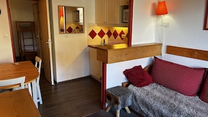 A compact living space with a kitchenette, a dining area, and a sofa with red pillows. - T2-6pers-34m2-quartier Bergers-pied des Pistes (Huez)