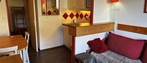 Ein kompakter Wohnbereich mit Küchenzeile, Essbereich und einer Couch mit roten Kissen.