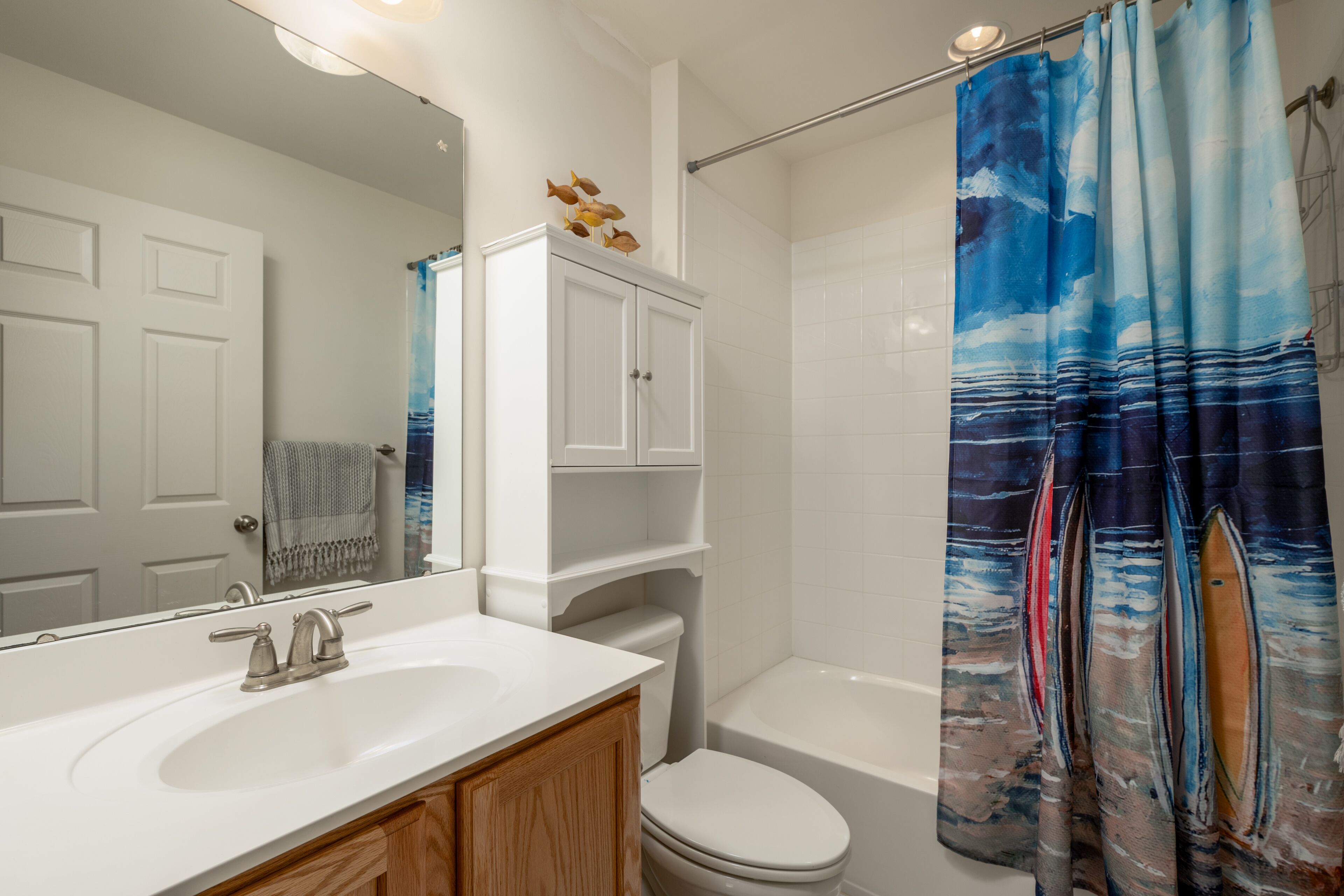 A bathroom with a white sink, wooden cabinets, a toilet, and a shower curtain with a nautical theme.