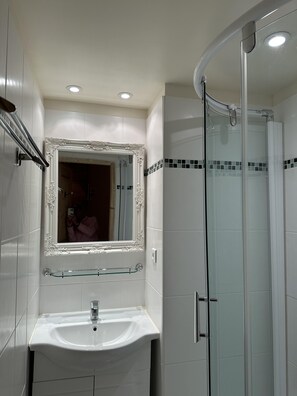 Bathroom features a glass shower enclosure, white sink, and mirror with ornate frame.