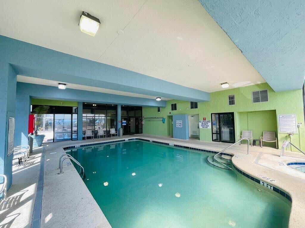 En swimmingpool med klart vatten, omgiven av en färgskala i blått och grönt, och ett område med sittplatser och stolar.