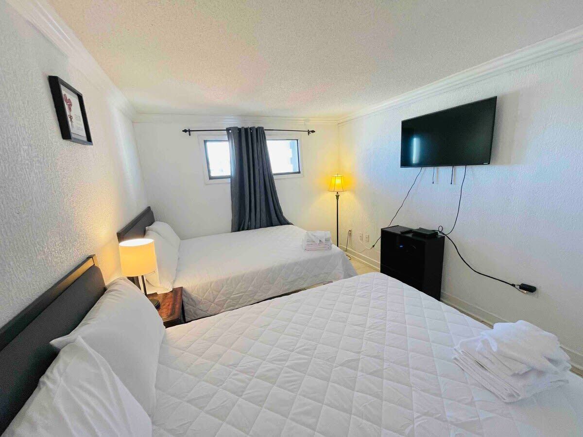 A hotel room with two beds, a TV, a lamp, and a window with curtains.