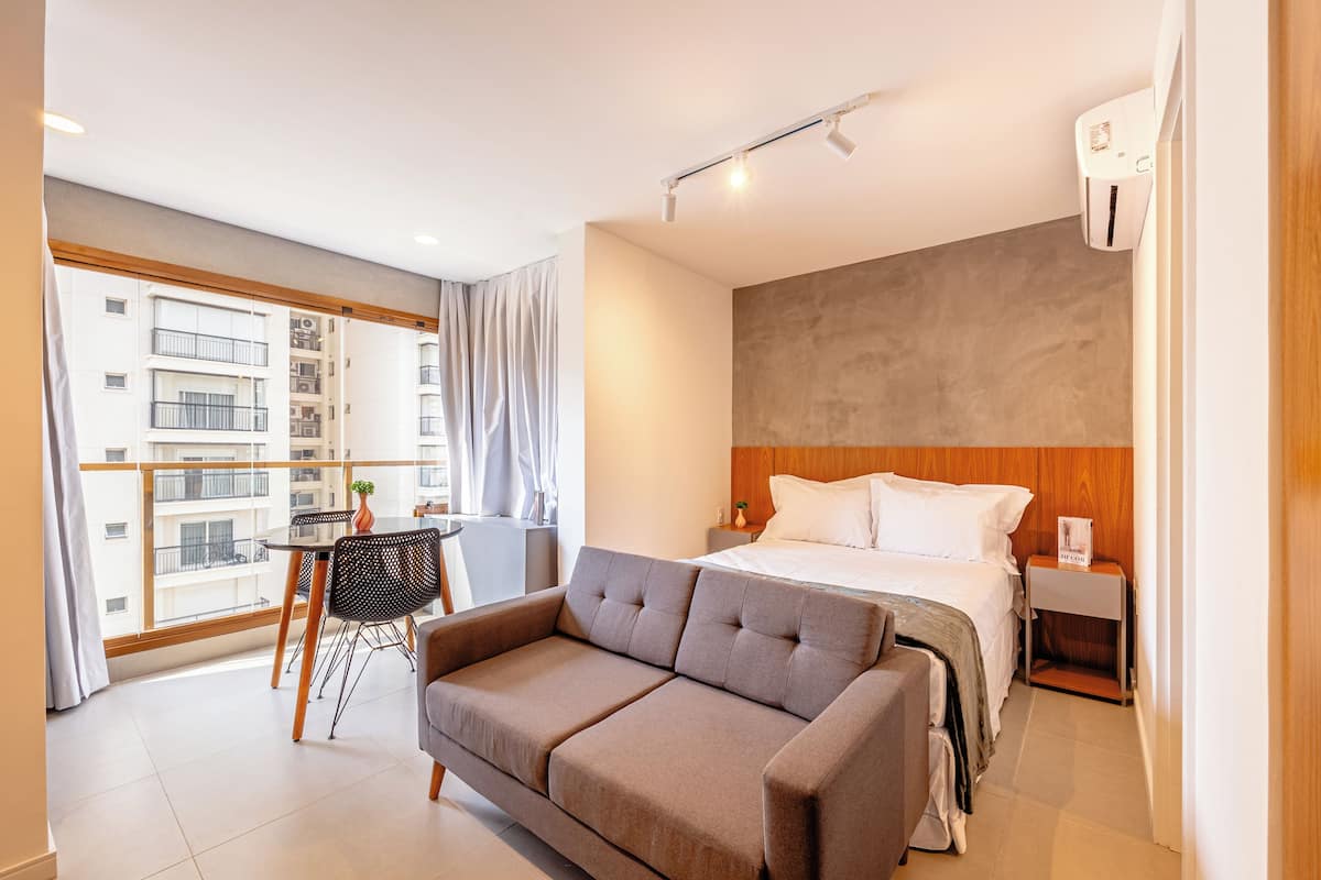 Ein Hotelzimmer mit einem Bett, einer Couch, einem kleinen Tisch und einem Balkon mit Blick auf andere Gebäude.