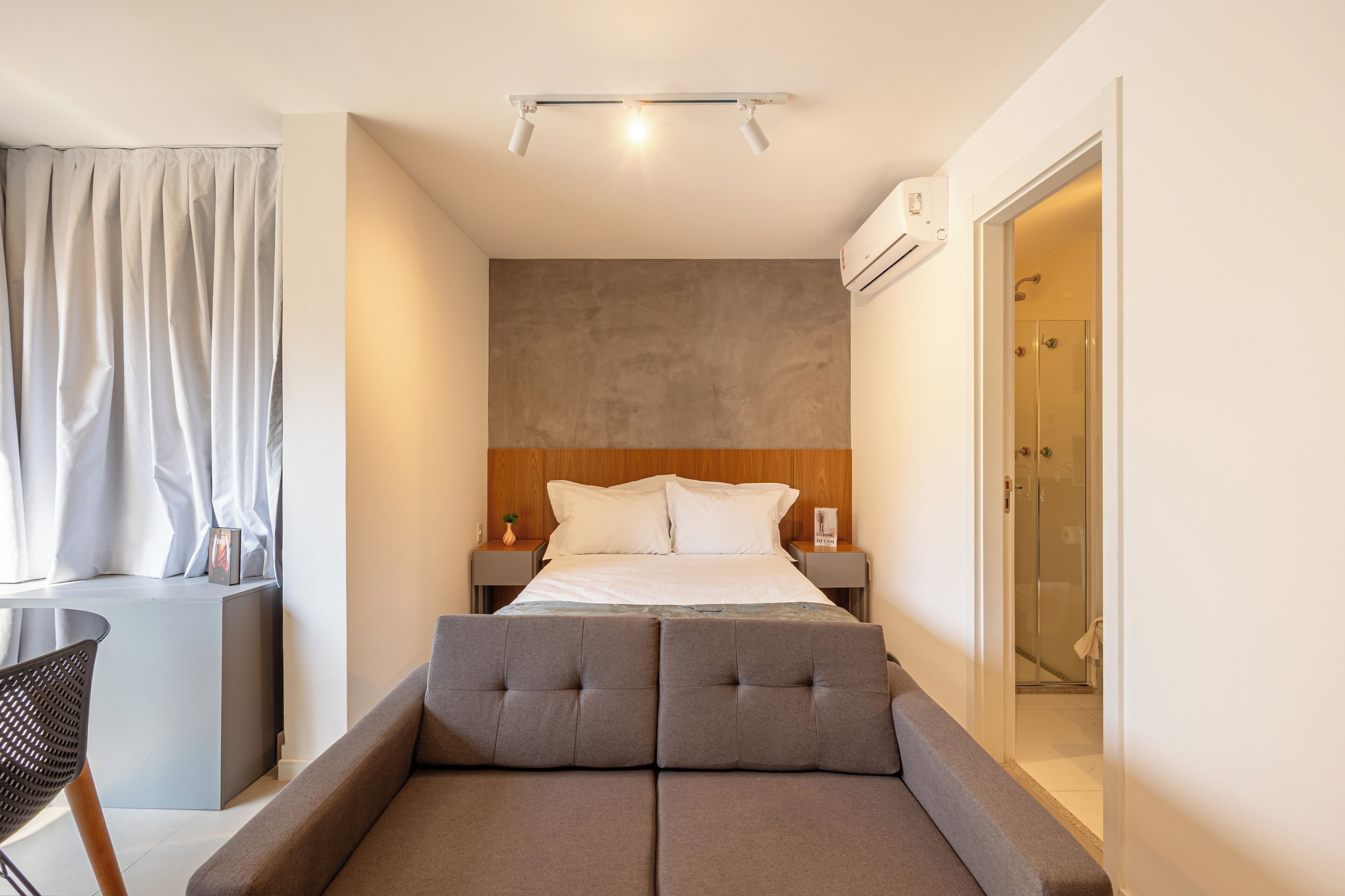 A modern hotel room with a large bed, a small desk, and a shower area.