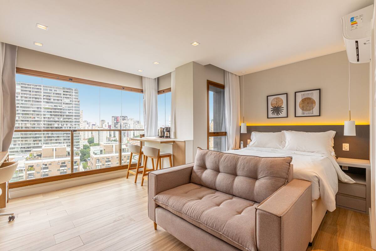 Ein modernes Hotelzimmer mit großem Fenster, einer Couch, einem Bett, einem Schreibtisch und Blick auf die Stadt.