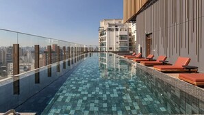 A rooftop infinity pool with a glass barrier, red lounge chairs, and a cityscape view. - DVN - D'Oru Vila Nova Conceição by Anora (São Paulo)