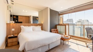 A modern hotel room with a large bed, a wooden nightstand, a chair, and a balcony with a city view. - DVN - D'Oru Vila Nova Conceição by Anora (São Paulo)