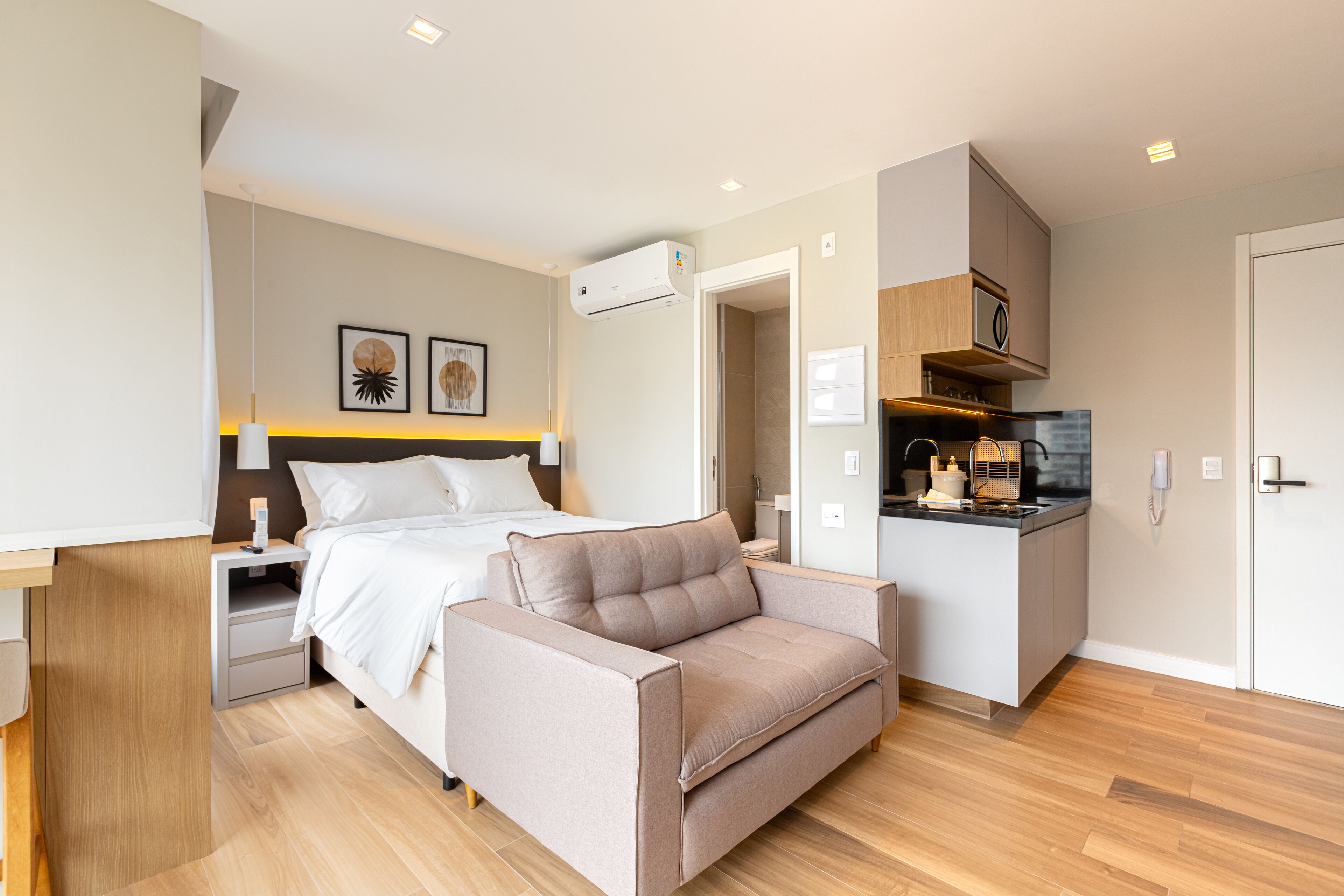 A modern hotel room with a bed, a sofa, a small kitchenette, and a bathroom.