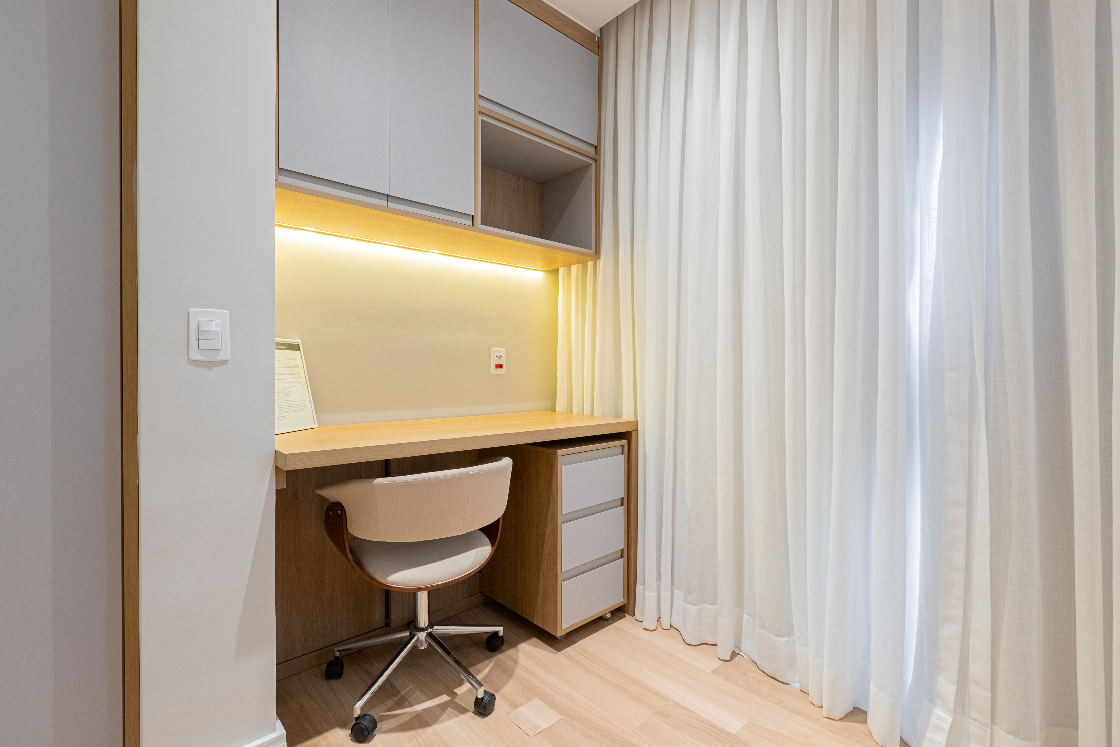 A modern bedroom with a wooden desk, a chair, and a bedside table.