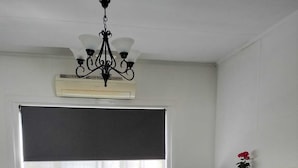 Un salon avec un canapé en cuir noir, un fauteuil en cuir noir, une petite table sur laquelle est posé un vase de fleurs rouges, un lustre noir et une grande fenêtre avec un store noir.
