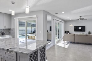A modern kitchen with a marble countertop, a dining area with a table and chairs, a sofa, and a TV mounted on the wall.