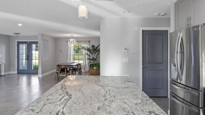 Een moderne keuken met een groot marmeren eiland, roestvrijstalen apparatuur en hangende lampen.