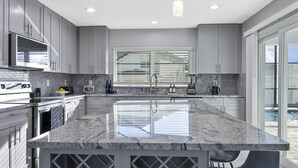 Een moderne keuken met grijze kastjes, een groot eiland met een spoelbak, en uitzicht op een zwembad door het raam.