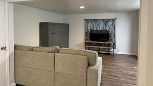 Een woonkamer met een hoekbank, een televisie op een dressoir en een kledingkast.