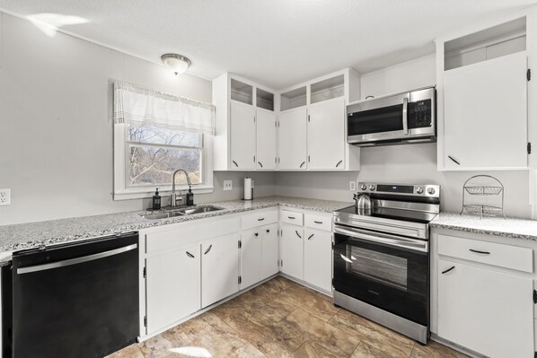 A modern kitchen with white cabinets, a stainless steel microwave, an oven, and a dishwasher.