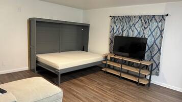 Una habitación pequeña con cama, televisor sobre un atril de madera y cortina estampada.