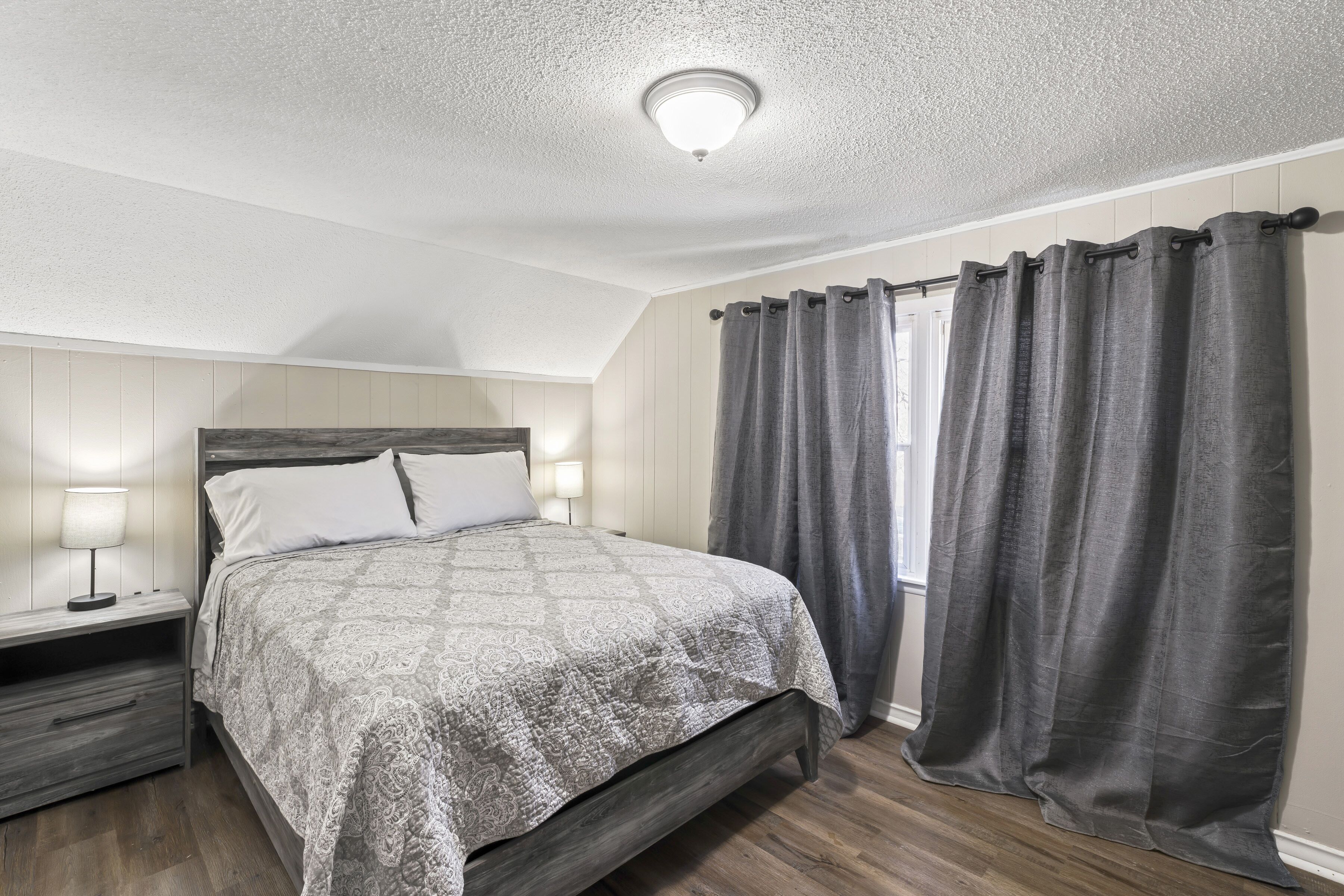 Une chambre à coucher avec un lit, des tables de chevet, une lampe et une fenêtre avec des rideaux.