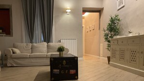 Ett vardagsrum med en beige soffa, en svart kista med klistermärken, en krukväxt och ett skåp med luckor med horisontella ribbor.
