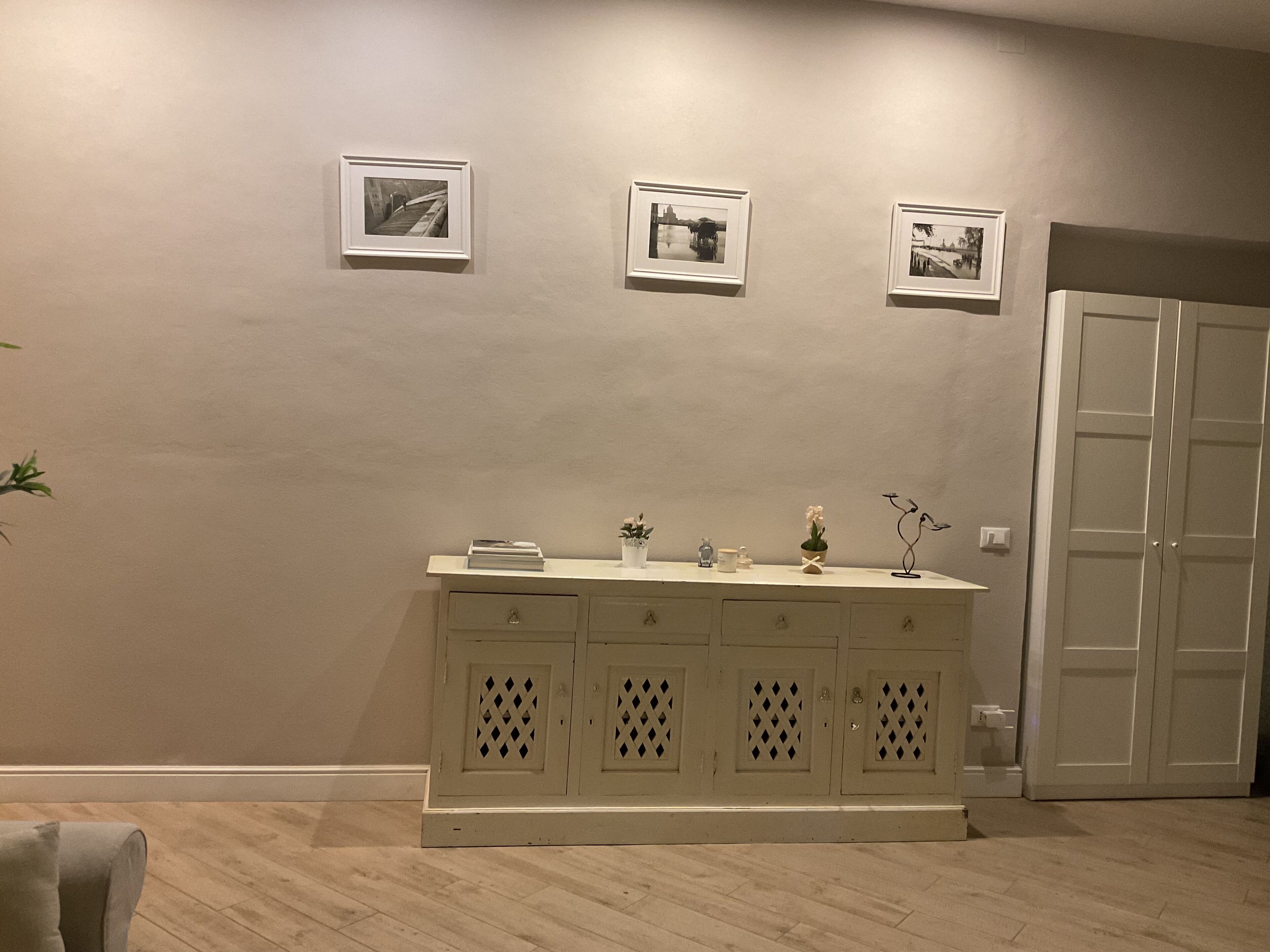 A room with a light-colored wooden floor, a white cabinet with decorative cutouts, and three framed pictures on the wall.