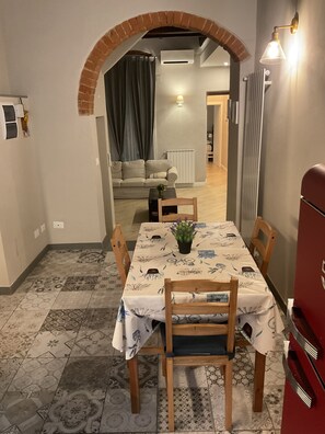 Uma área de refeições com uma mesa posta para quatro pessoas, uma planta em vaso e um eletrodoméstico vermelho ao fundo.