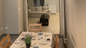 Ett mysigt vardagsrum med en soffa, ett matbord med stolar och ett litet bord med en växt. En välvd dörröppning leder till ett annat rum med ett element och gardiner.