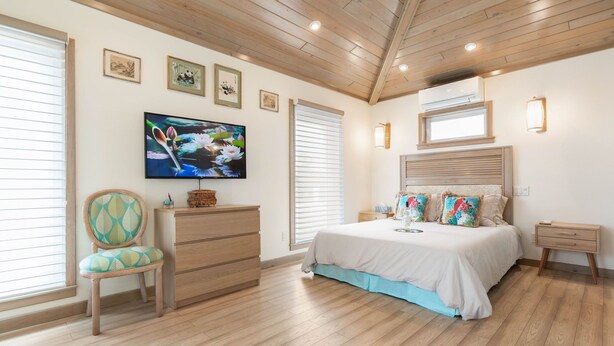 A bedroom with a bed, dresser, chair, and a TV on the wall. - Beachside Cottage
 (Flagler Beach)