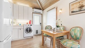 A compact kitchen with a washing machine, a dining table with chairs, and a window with blinds. - Beachside Cottage
 (Flagler Beach)